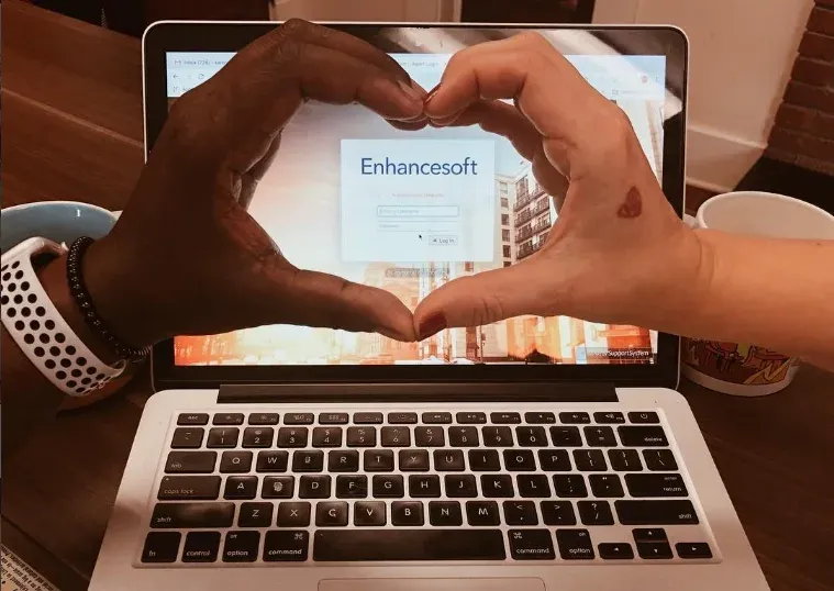 Two Enhancesoft team members forming a heart around a laptop